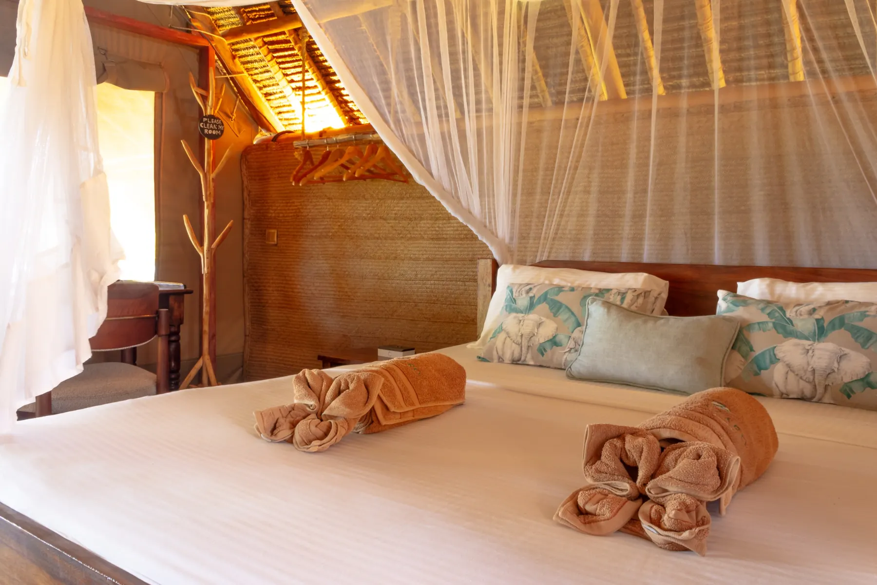 Canopy bed with rolled towels under a makuti roof