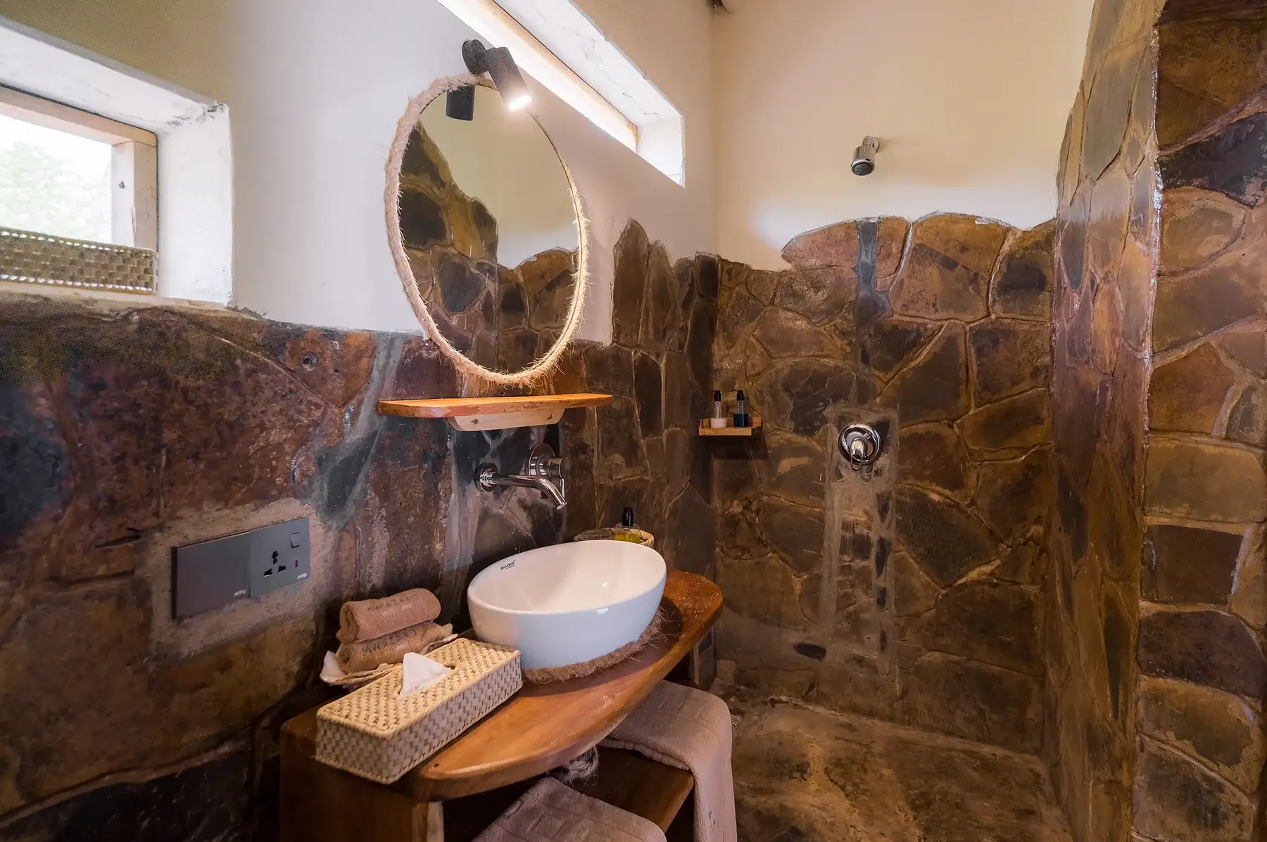 Stone bathroom with round mirror and walk-in shower